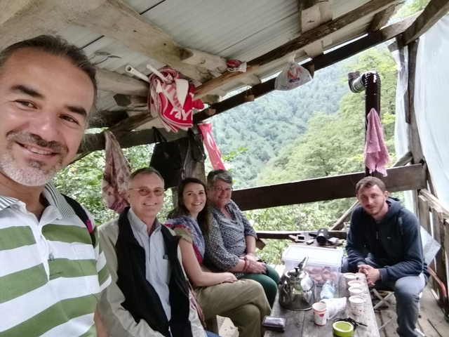 A group of people in a rustic wooden outdoor setting overlooking lush greenery.