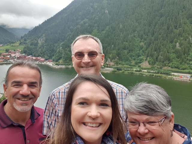 A group selfie with a scenic view of a lake and green hills.