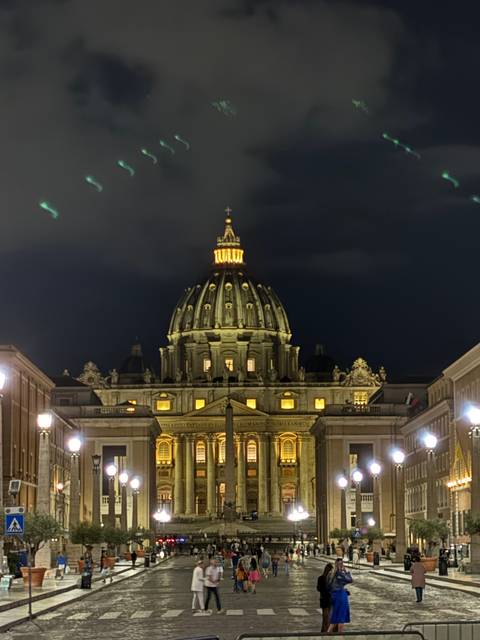       Illuminated basilica at night with people in the foreground.
  