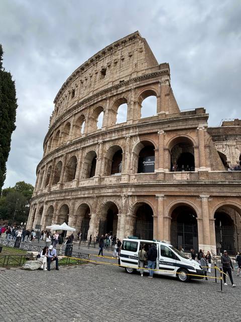      Exterior view of the Colosseum with tourists nearby.
  