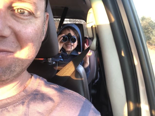 Person in front seat of a vehicle with a child visible through the rearview mirror.