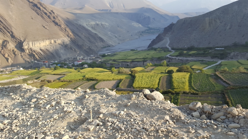       Wide view of a valley with green fields and mountains.
  