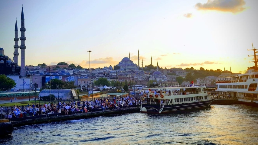 Busy harbor area with boats and mosque towers in the background.