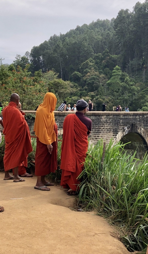       A group of monks in red robes near a bridge.
  