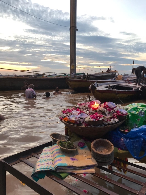       Flowers and candles on a river with people performing rituals.
  