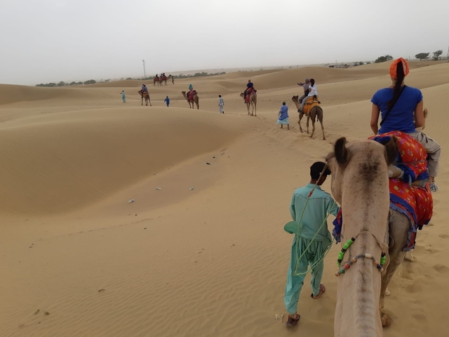       People riding camels across a vast sand dune landscape.
  
