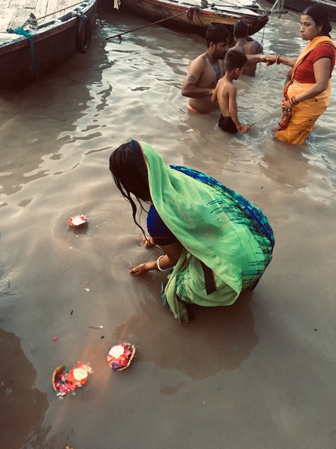 Woman performing a ritual in a river, wearing a green saree.