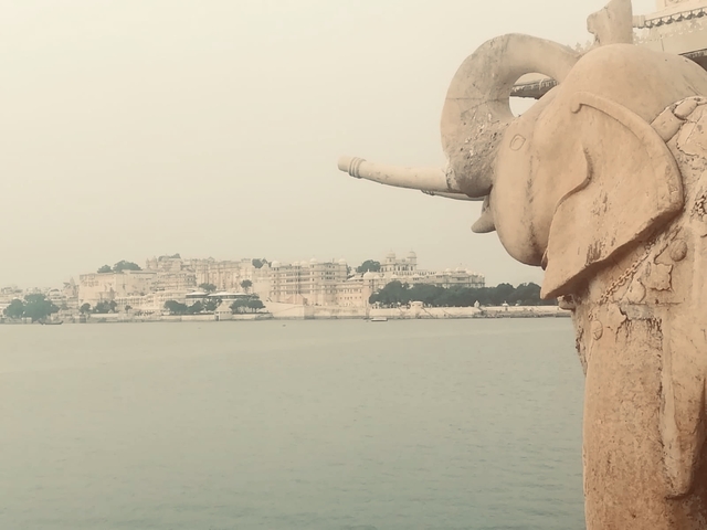 Elephant statue by a lake with a cityscape in the background.