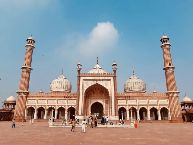       Majestic building with domes and minarets, likely a mosque, with people in front.
  