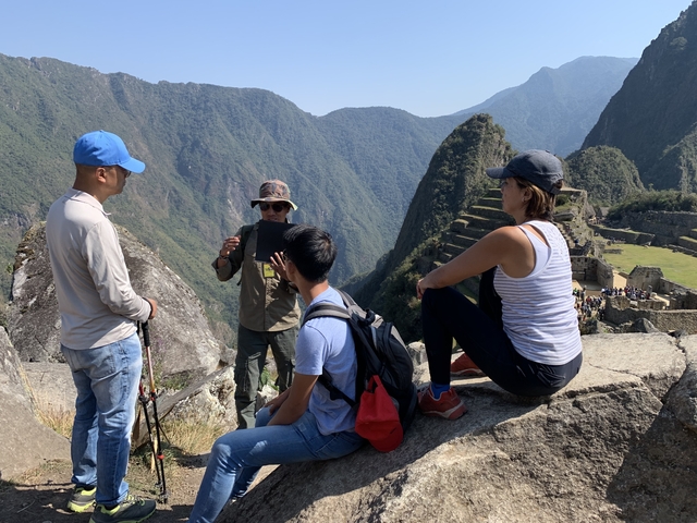       Group of people hiking among ancient Inca ruins with mountains.
  