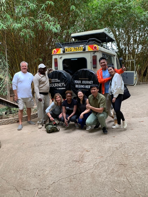       Group of people posing in front of a safari van with 'National Geographic Journeys' written on spare tire covers.
  