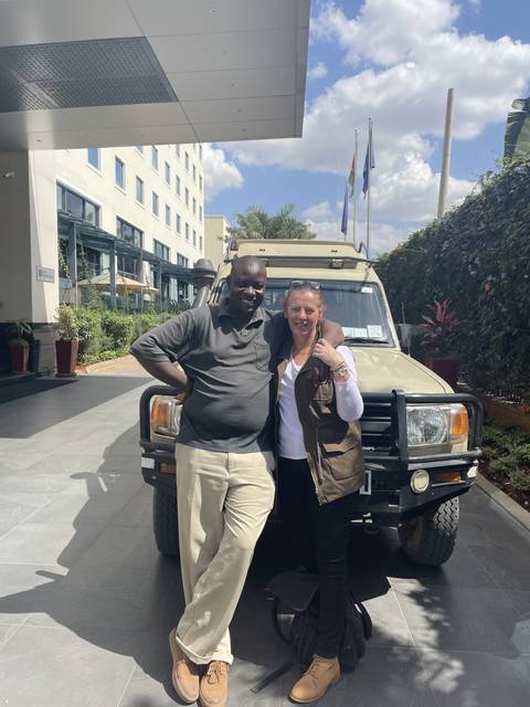       Two people posing in front of a safari vehicle at a lodge.
  