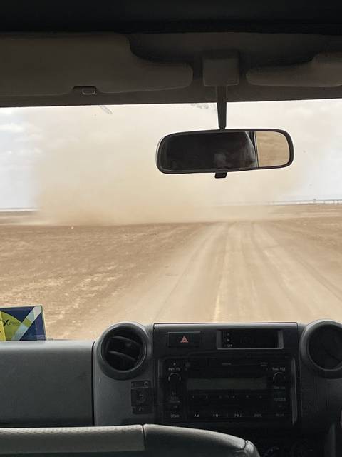 View of a vehicle's interior and dusty road.