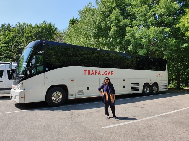 Person standing beside a large tour bus in a leafy area.