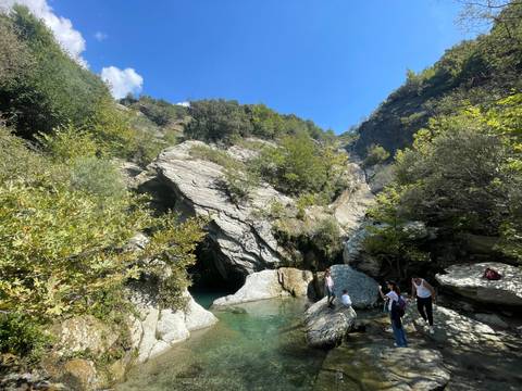 People by a rocky river surrounded by trees and cliffs.