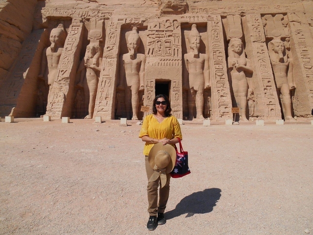 Person posing at the entrance of a temple with carvings of Egyptian gods.