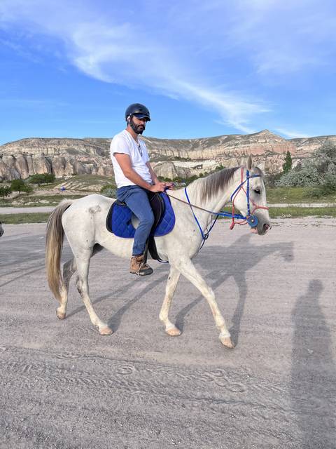 Person riding a white horse in a rocky landscape.
