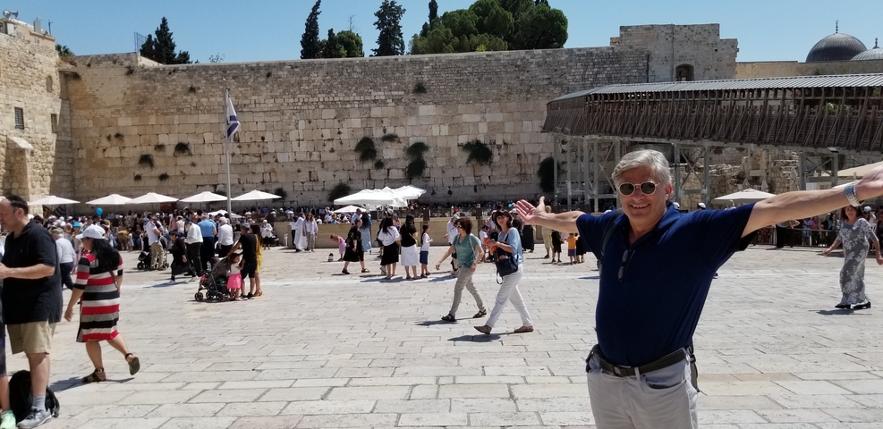 Man posing with arms outstretched in front of the Western Wall.