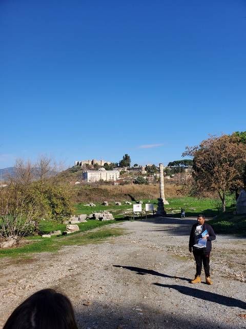       Ruins of an ancient site with a person walking and columns standing.
  