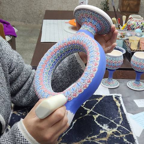       Close-up of an intricately painted ceramic artwork being held.
  
