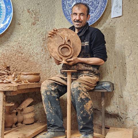       Man holding a clay pot in a pottery setting.
  
