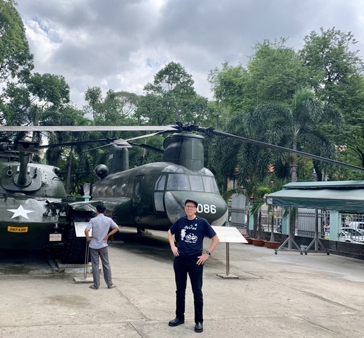 A man standing in front of a military helicopter displayed outdoors.