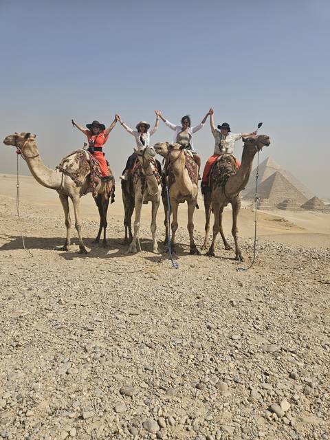 Four people riding camels in a desert near pyramids.