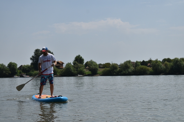 Man paddleboarding on calm waters with trees in the background.