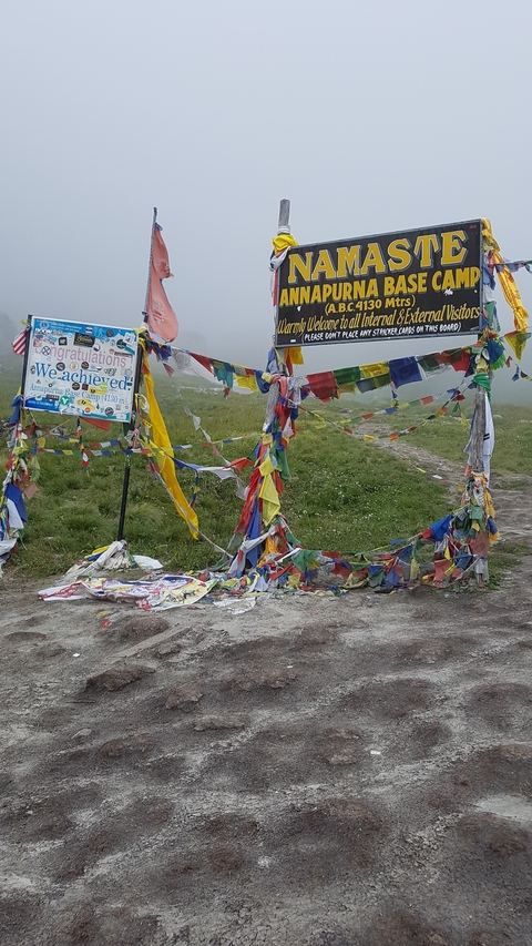 Prayer flags and a congratulatory sign at a base camp with people nearby.