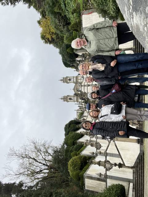 Group of people posing in front of a historical building with a garden.