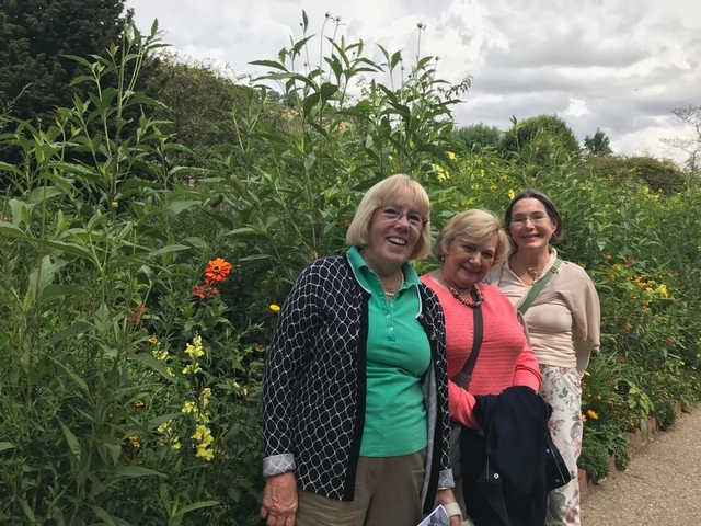 Three women standing in a colorful garden.