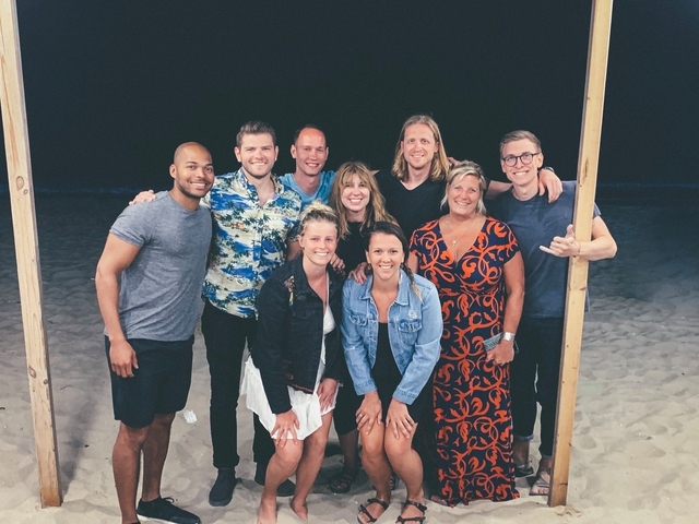       Group of people posing together on a beach at night.
  