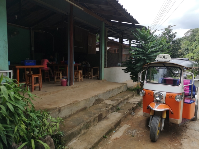 Tuk-tuk parked outside a small restaurant with people inside.