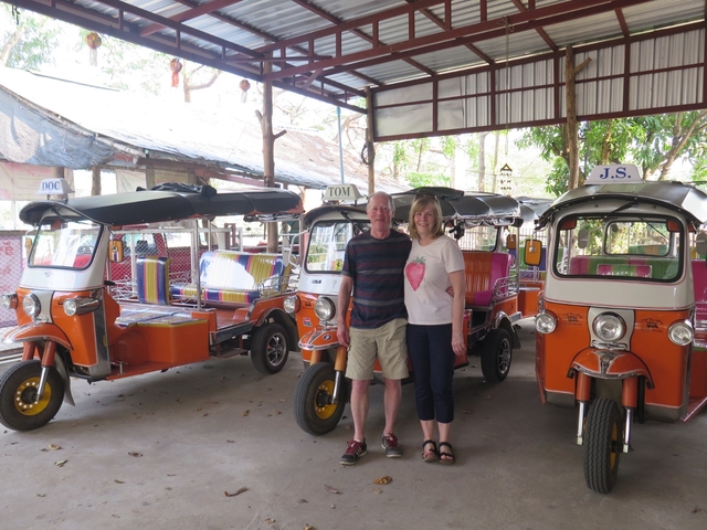       Two people standing in front of a row of tuk-tuks.
  