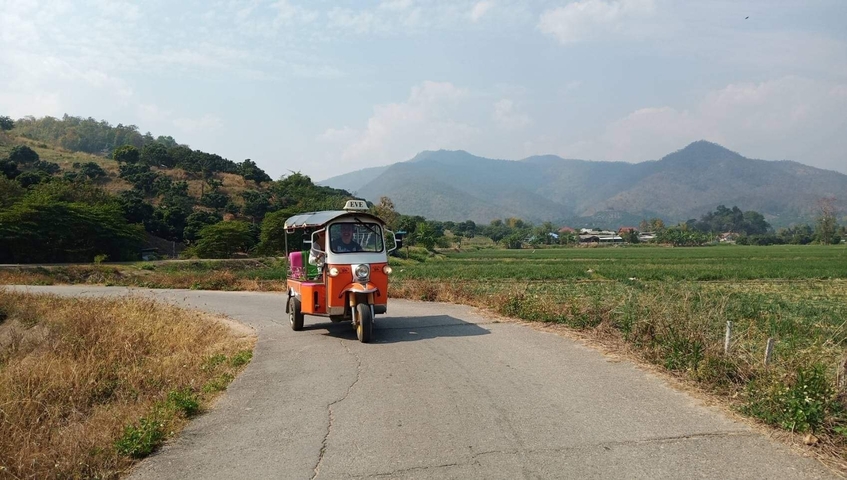 Tuk-tuk driving along a rural road with mountains in the background.