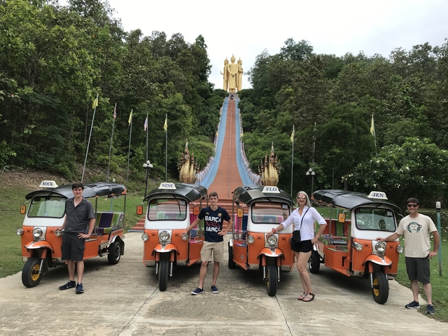 Tour group posing with tuk-tuks in front of a large Buddha statue on a hill.