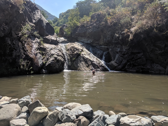       Person swimming in a small pool below a waterfall.
  