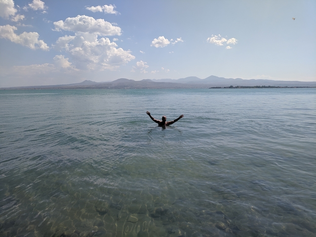       Person submerged in a lake surrounded by mountains in the distance.
  