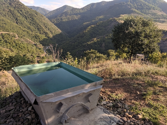       Metal trough filled with water overlooking a lush valley.
  