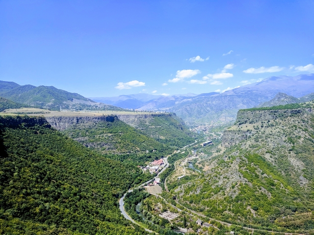       Expansive view of lush valleys and mountains under a clear blue sky.
  
