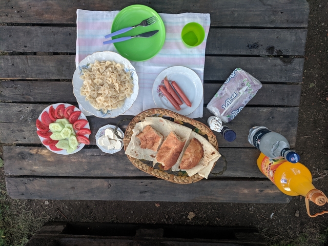       Outdoor picnic setting with a variety of food on a wooden table.
  