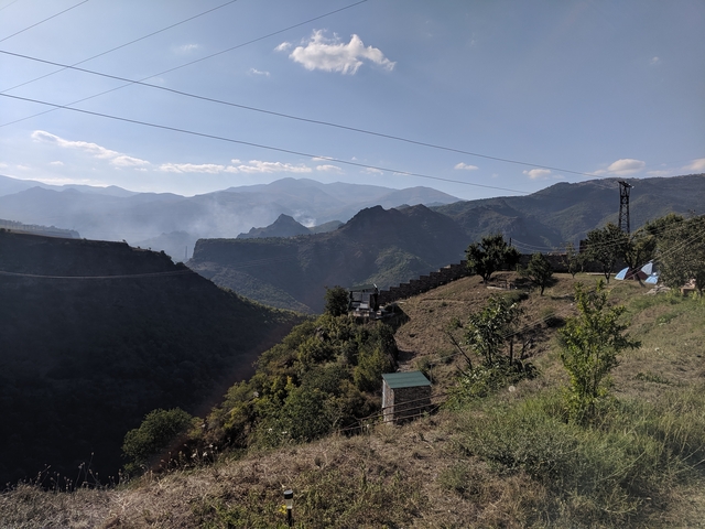       Overlooking a mountain landscape with scattered vegetation and smoke in the air.
  