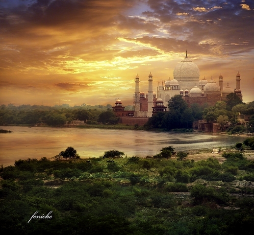       Majestic view of the Taj Mahal across a reflective river during a colorful sunset.
  