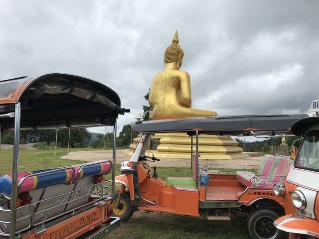 Golden Buddha statue and tuk-tuks under cloudy sky.
