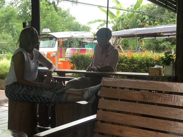 Two people sitting at an outdoor table near tuk-tuks.