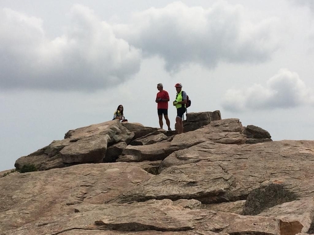 Three people standing on rocky terrain with clouds in the background.