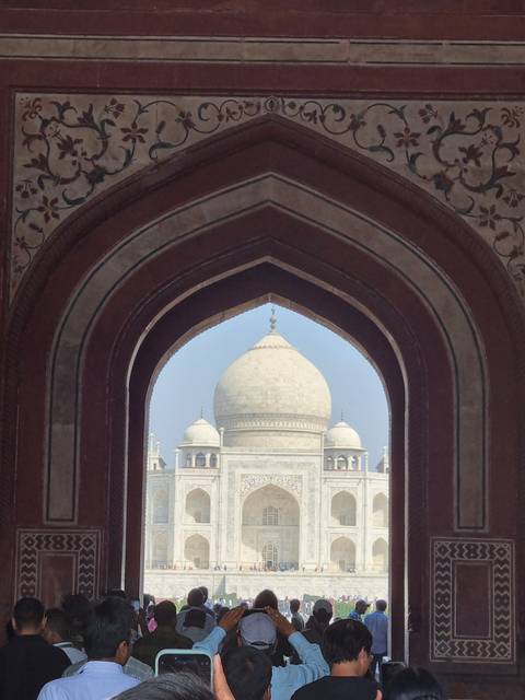       Taj Mahal viewed through an archway with visitors present.
  