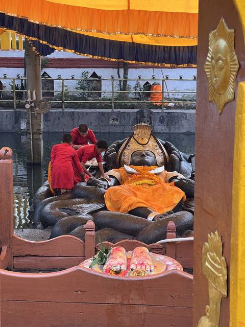       Monks attending to a golden statue under an orange canopy.
  