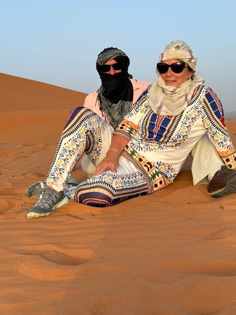 Two people sitting on desert sand wearing traditional clothes.