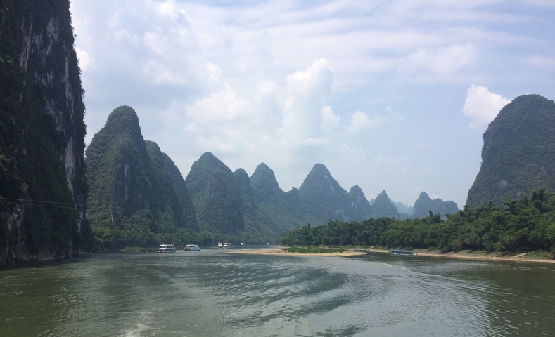 River surrounded by karst mountains under a cloudy sky.